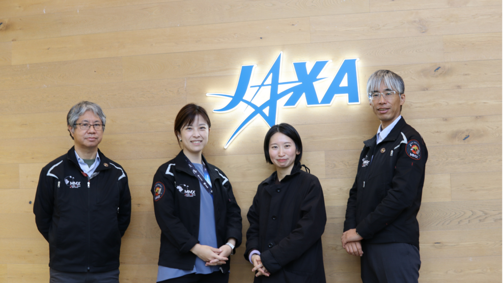 JAXAのロゴの前でMMXミッションマークプロジェクトの皆さんが並んでいる様子。左からJAXA矢治氏、JAXA宮崎氏、小林氏、JAXA馬場氏